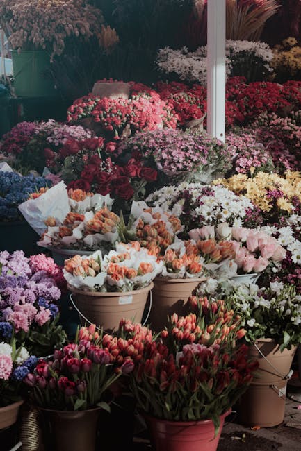 A vibrant array of flower arrangements at a florist display, featuring a variety of fresh flowers including tulips, chrysanthemums, and carnations in shades of pink, red, purple, and white. The flower