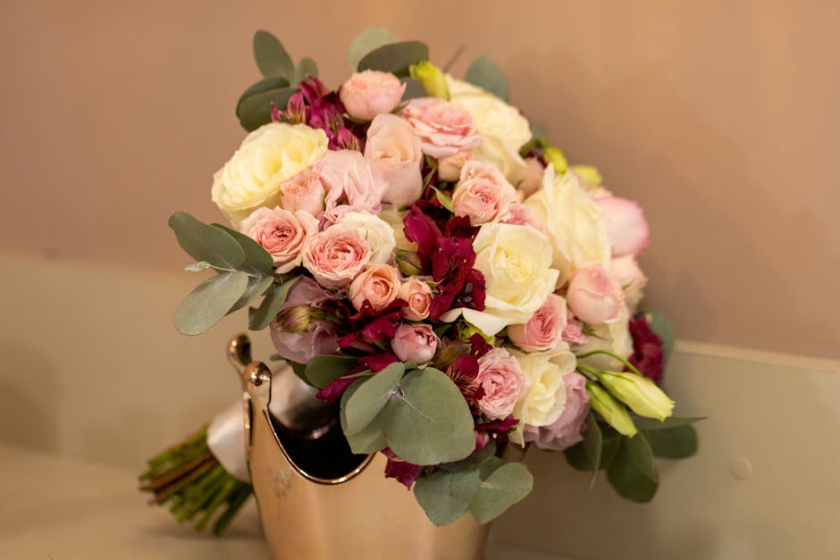 A close-up of a floral bouquet featuring light pink roses, white lisianthus, and deep burgundy flowers, all arranged with green eucalyptus leaves. The flowers are fresh with delicate, layered petals a
