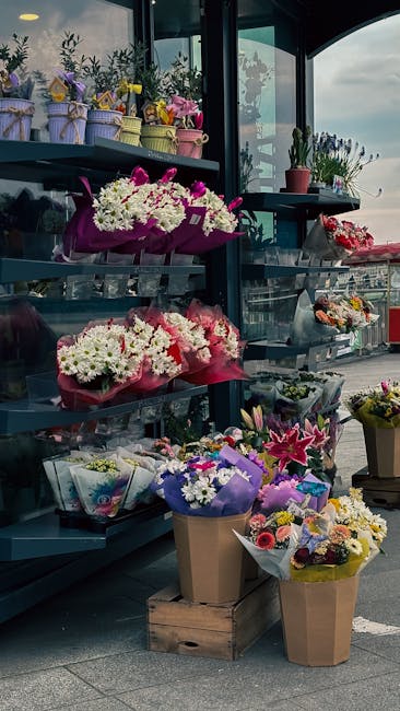 A display of various fresh flower arrangements showcased on a blue shelving unit at a florist, featuring bouquets of predominantly white, pink, and purple flowers wrapped in colorful paper and celloph